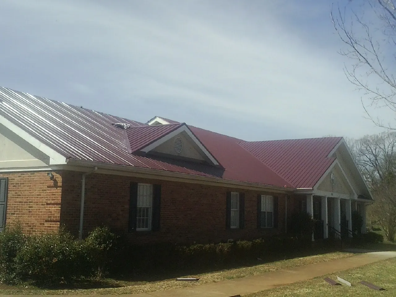 Red metal roof with gabled entries on a long brick building, from a Hail Damage Roof Repair job in Rogers