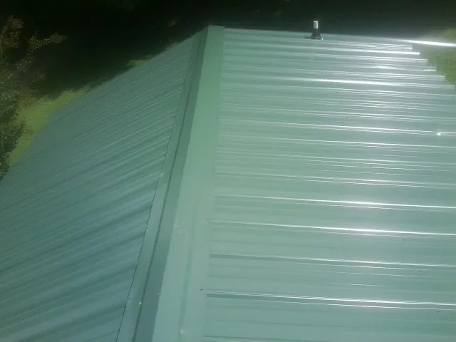 New green metal panels meeting at the ridge of a roof — Flat Roof Repair work by our crew in Rogers